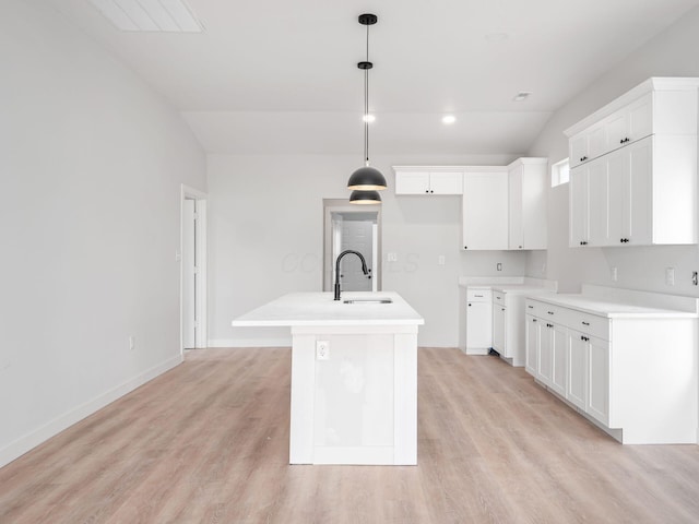 kitchen featuring light hardwood / wood-style floors, decorative light fixtures, vaulted ceiling, a kitchen island with sink, and white cabinets