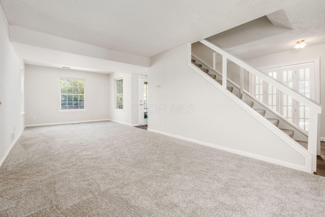 unfurnished room featuring carpet, a textured ceiling, stairway, and baseboards