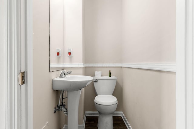 half bathroom featuring a sink, wood finished floors, toilet, and baseboards