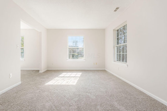 carpeted empty room with baseboards, visible vents, and a healthy amount of sunlight