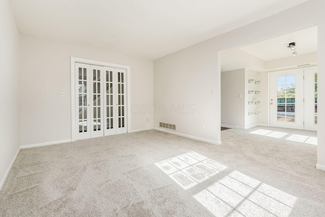 carpeted empty room with french doors, visible vents, and baseboards