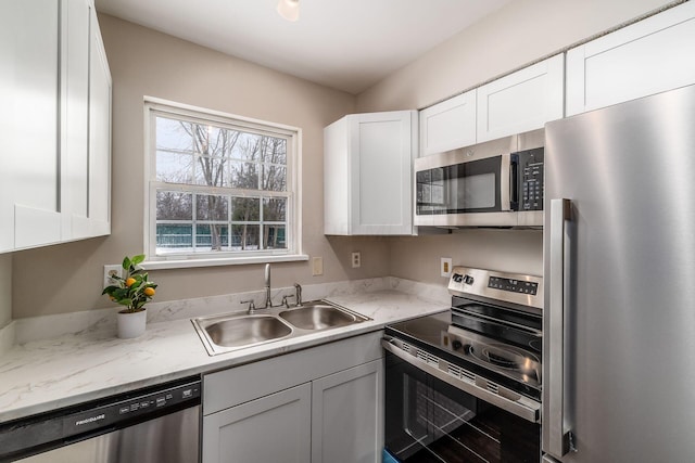 kitchen featuring light stone counters, appliances with stainless steel finishes, a sink, and white cabinetry