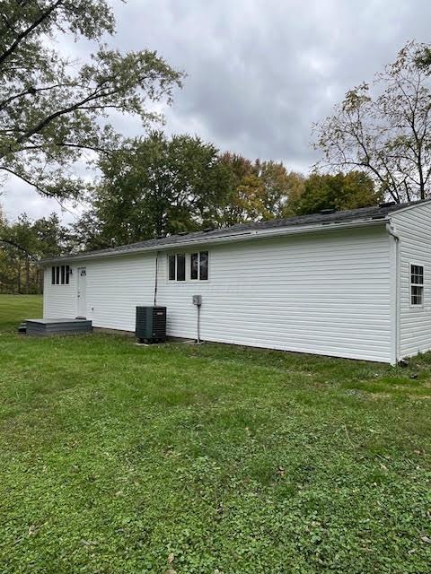 rear view of property with cooling unit and a lawn