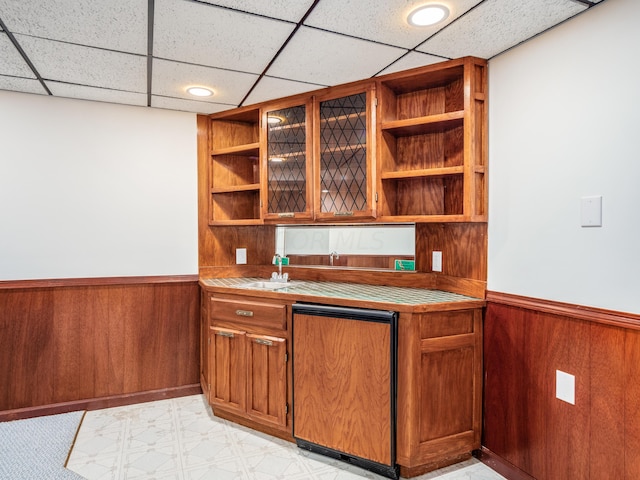 bar featuring a drop ceiling, refrigerator, and wooden walls