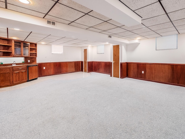 basement featuring a paneled ceiling, light colored carpet, wooden walls, and sink