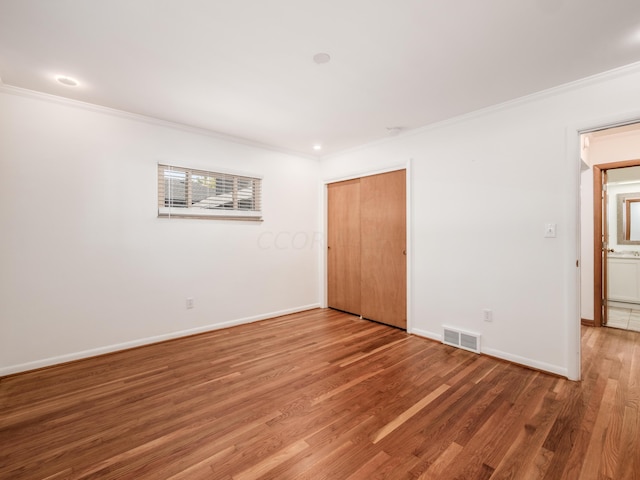 unfurnished bedroom featuring wood-type flooring, ornamental molding, and a closet