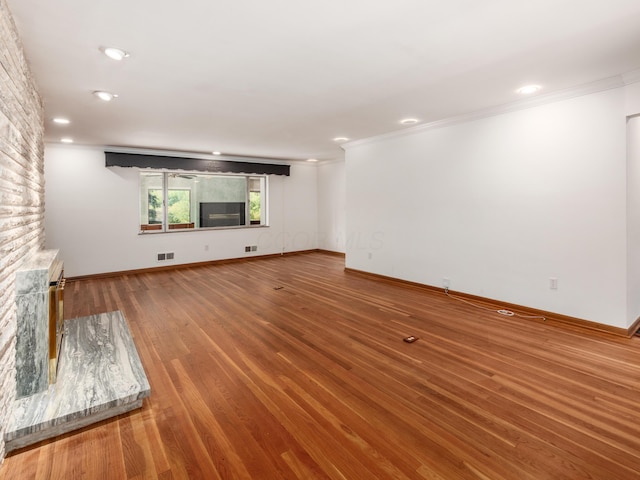 unfurnished living room with wood-type flooring, crown molding, and a brick fireplace