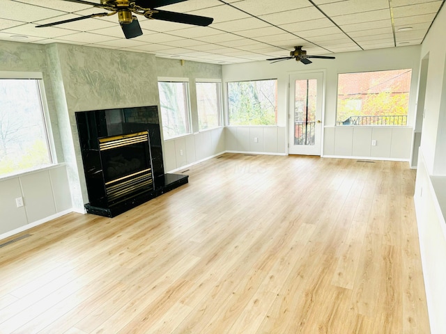 unfurnished living room featuring a wealth of natural light, a drop ceiling, and light hardwood / wood-style floors