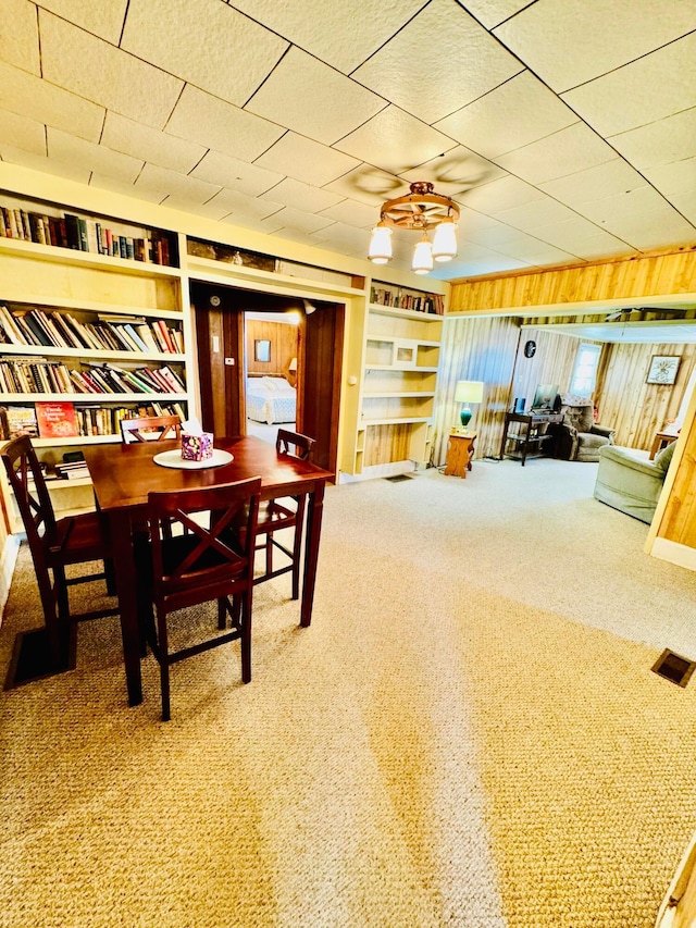 carpeted dining area featuring ceiling fan and wooden walls