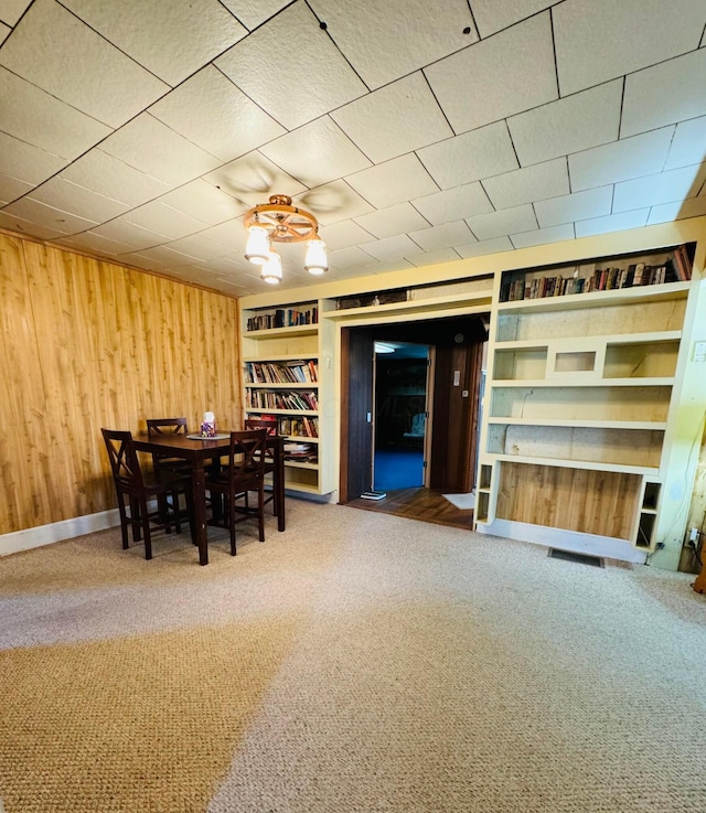 unfurnished dining area with built in shelves, wood walls, and carpet