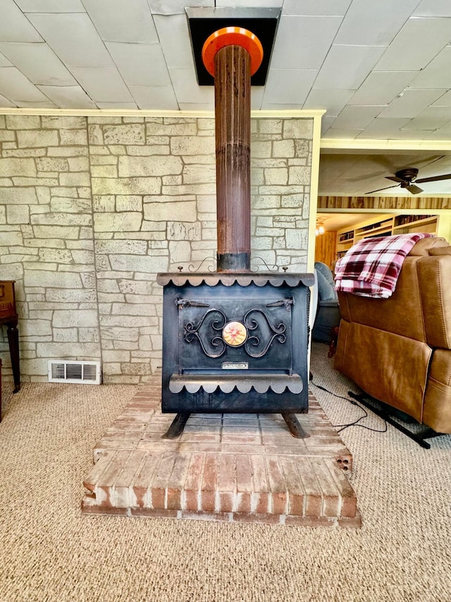 room details featuring carpet flooring, a wood stove, and ceiling fan