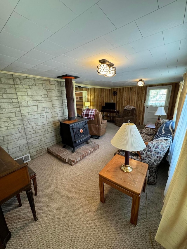 carpeted living room featuring a wood stove and wooden walls