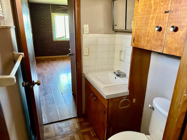 bathroom featuring parquet floors, vanity, toilet, and tile walls