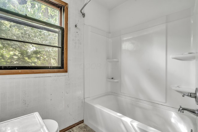 bathroom with toilet, tile walls, and tub / shower combination