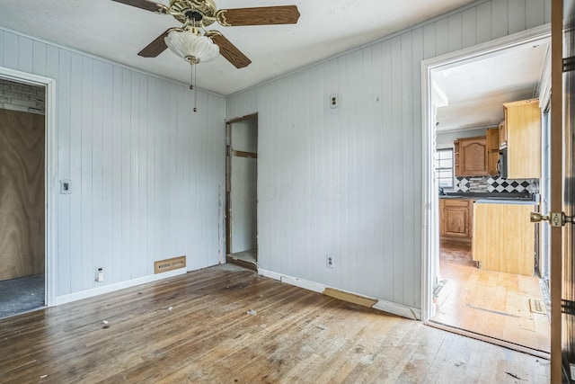 unfurnished room with wooden walls, hardwood / wood-style floors, and ceiling fan