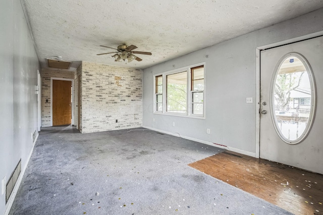 carpeted foyer entrance with ceiling fan, a textured ceiling, and brick wall