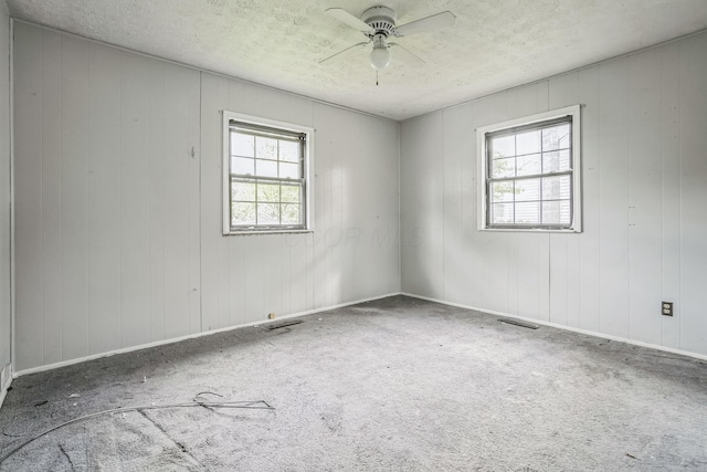 carpeted empty room with wooden walls, ceiling fan, a textured ceiling, and a wealth of natural light