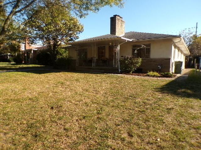 back of house with a yard, a chimney, and stucco siding