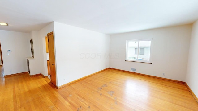 empty room with light wood-style floors, visible vents, and baseboards