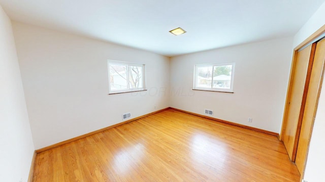 unfurnished bedroom with light wood-type flooring, visible vents, and multiple windows