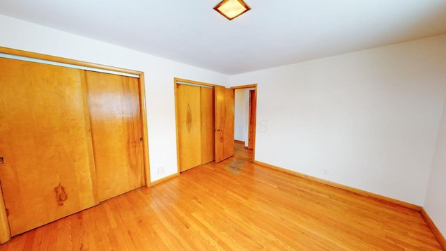 unfurnished bedroom with two closets, baseboards, and light wood-style floors