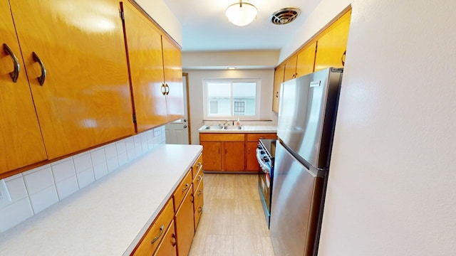 kitchen featuring visible vents, freestanding refrigerator, a sink, light countertops, and backsplash