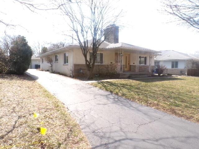 ranch-style home featuring stucco siding, aphalt driveway, a porch, a front yard, and a chimney