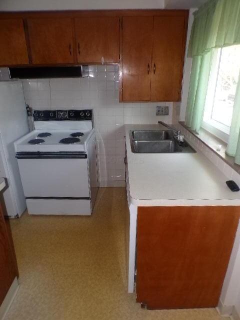 kitchen with white appliances, brown cabinetry, a sink, light countertops, and under cabinet range hood