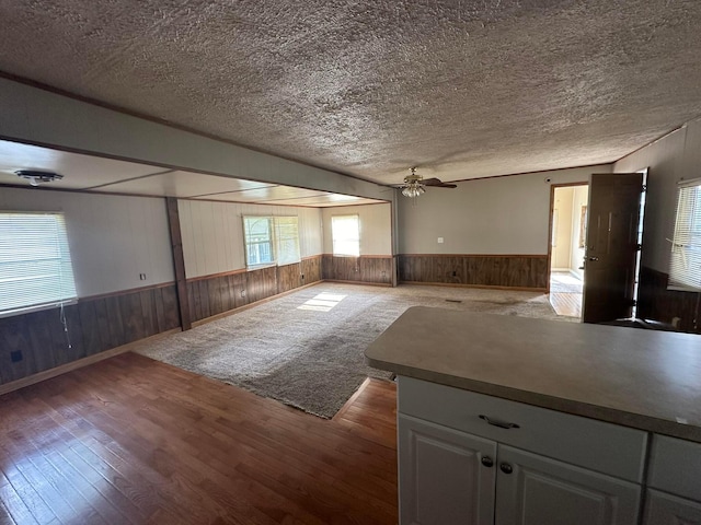 empty room featuring a textured ceiling, ceiling fan, wooden walls, and dark hardwood / wood-style floors