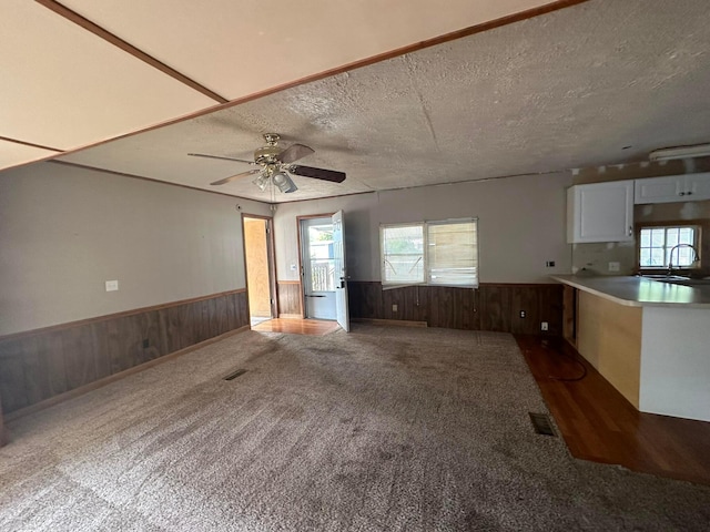 unfurnished living room featuring wooden walls, ceiling fan, dark carpet, and a textured ceiling