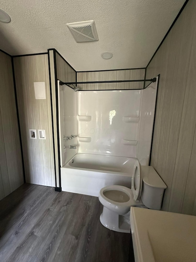 full bathroom with hardwood / wood-style flooring, toilet, tub / shower combination, and a textured ceiling