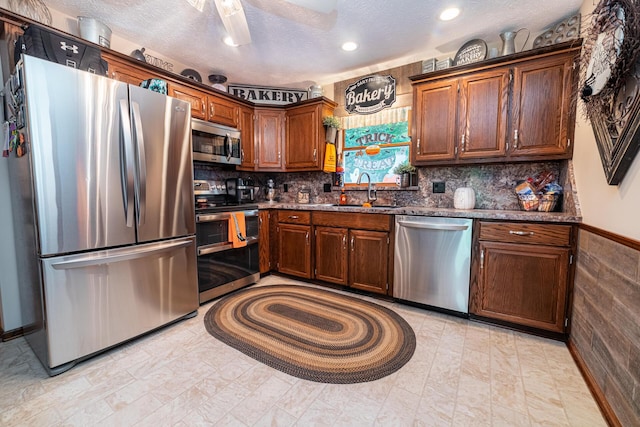 kitchen with sink, a textured ceiling, dark stone countertops, and appliances with stainless steel finishes