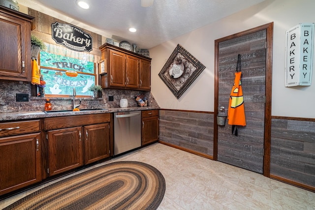 kitchen with sink, dark stone countertops, stainless steel dishwasher, and a textured ceiling