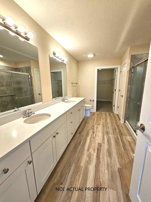 bathroom featuring a textured ceiling, toilet, an enclosed shower, vanity, and hardwood / wood-style flooring