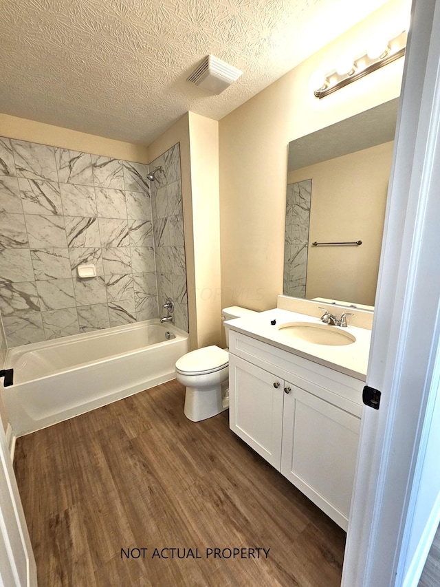 full bathroom featuring vanity, tiled shower / bath, hardwood / wood-style flooring, toilet, and a textured ceiling