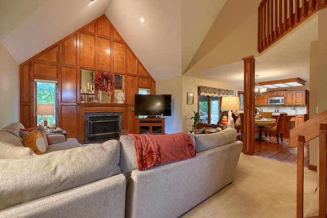 living room featuring light hardwood / wood-style flooring, high vaulted ceiling, a notable chandelier, decorative columns, and wooden walls