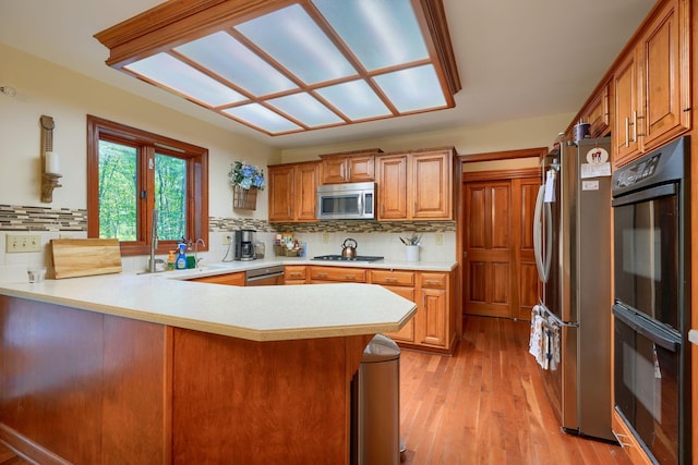 kitchen featuring backsplash, kitchen peninsula, light hardwood / wood-style flooring, and stainless steel appliances