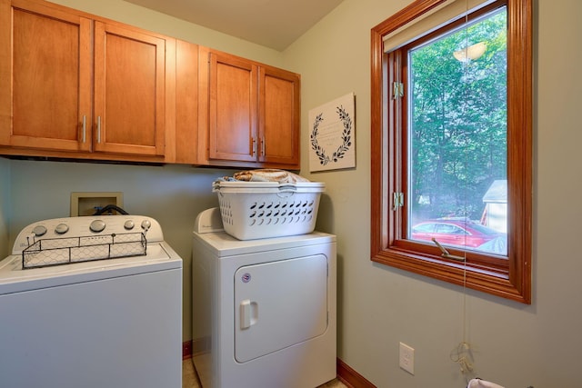 clothes washing area featuring a wealth of natural light, washer and clothes dryer, and cabinets