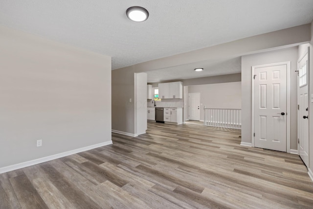 unfurnished living room featuring light hardwood / wood-style floors, sink, and a textured ceiling