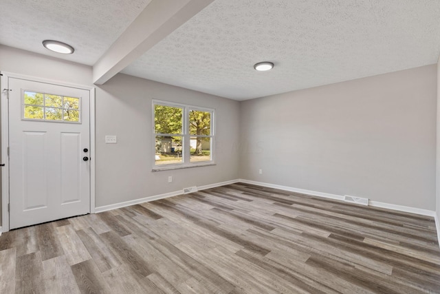 entrance foyer with plenty of natural light, beamed ceiling, a textured ceiling, and light hardwood / wood-style flooring