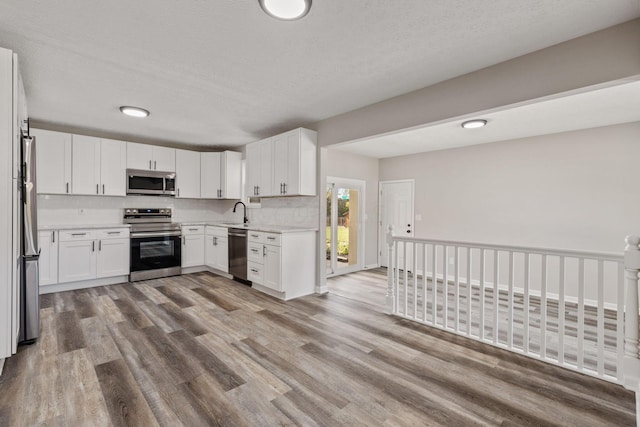 kitchen with white cabinets, tasteful backsplash, appliances with stainless steel finishes, and light hardwood / wood-style flooring