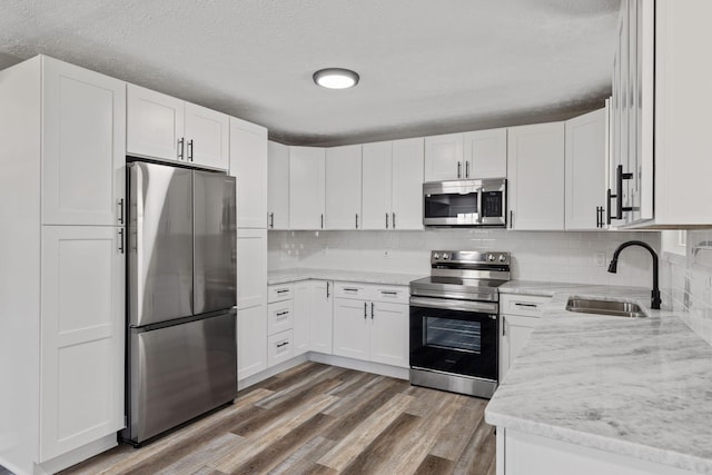 kitchen with light stone countertops, stainless steel appliances, sink, hardwood / wood-style floors, and white cabinetry