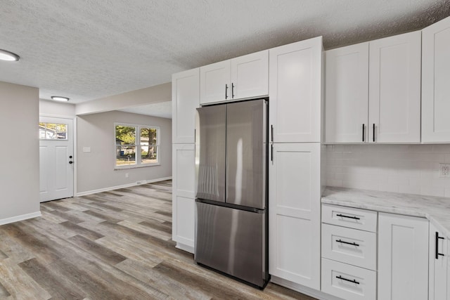 kitchen featuring white cabinets, light wood-type flooring, stainless steel refrigerator, and backsplash