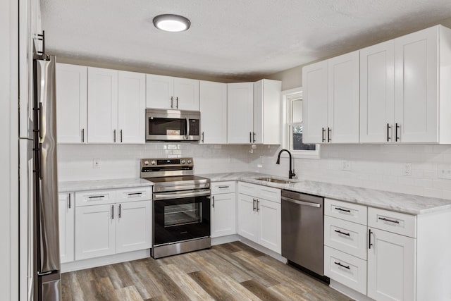 kitchen featuring a textured ceiling, stainless steel appliances, sink, white cabinets, and light hardwood / wood-style floors