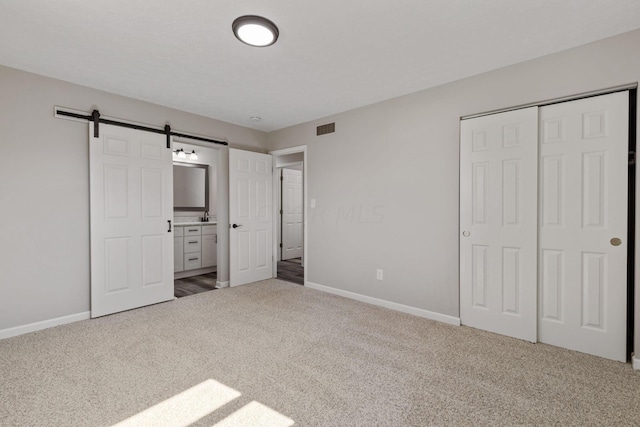 unfurnished bedroom with a barn door, carpet floors, a closet, and ensuite bath