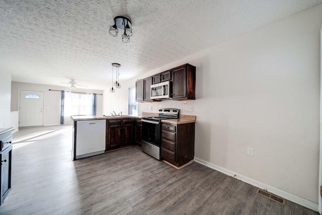 kitchen featuring stainless steel appliances, kitchen peninsula, hardwood / wood-style floors, a textured ceiling, and decorative light fixtures