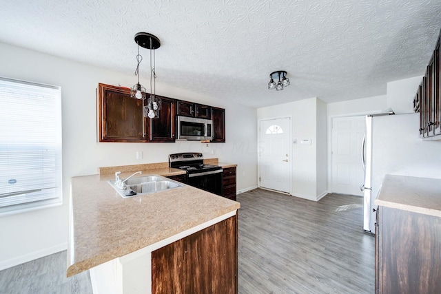 kitchen with kitchen peninsula, stainless steel appliances, sink, pendant lighting, and light hardwood / wood-style flooring