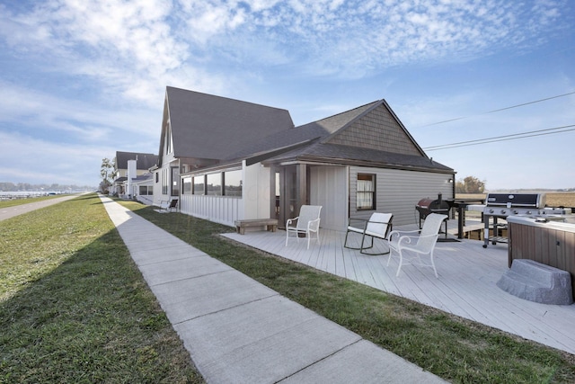 rear view of property featuring a lawn, a wooden deck, a sunroom, and a hot tub