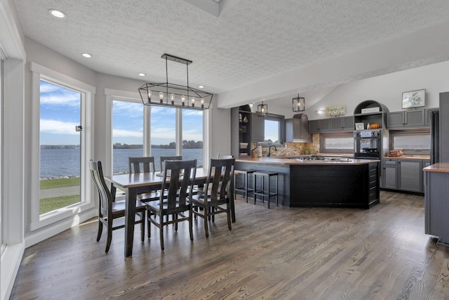 dining room with a textured ceiling, sink, a water view, and dark wood-type flooring