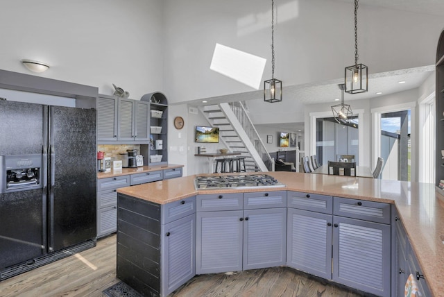 kitchen featuring black refrigerator with ice dispenser, light wood-type flooring, decorative light fixtures, and stainless steel gas stovetop